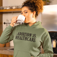 Army green feminist hoodie that says abortion is healthcare in black and pink hand lettered text- shop feminist apparel and pro choice tees