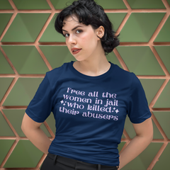 Navy blue feminist shirt that says free all the women in jail in lilac writing. Shop feminist apparel