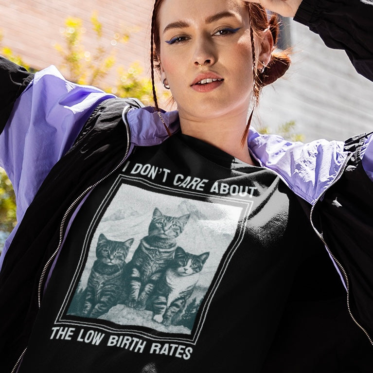black feminist tshirt that says I don't care about the low birth rates in light blue writing featuring a photograph of three sitting tabby cats- shop Feminist Trash for feminist tees, political clothing, dump him shirts and pride merch.