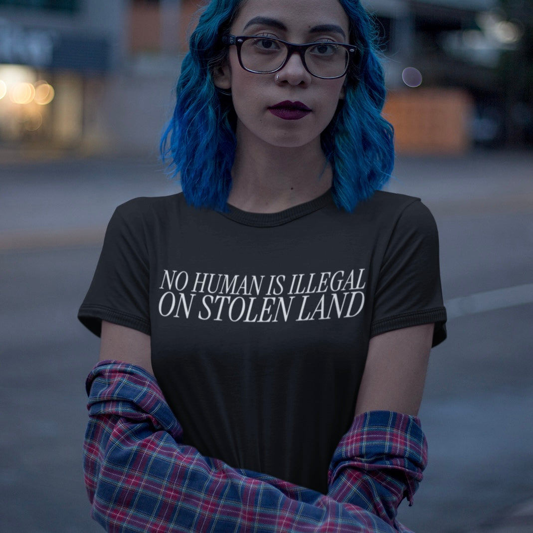 black political t-shirt that says no human is illegal on stolen land in white thin writing. Shop feminist trash store for political clothes and feminist shirts