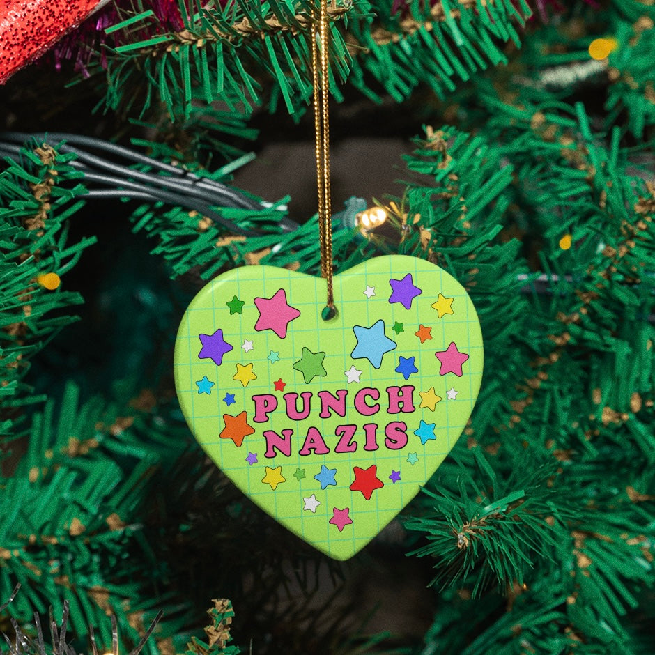 Heart shaped Christmas decoration that says punch Nazis in pink writing surrounded by colourful stars- shop feminist trash for political Christmas decorations