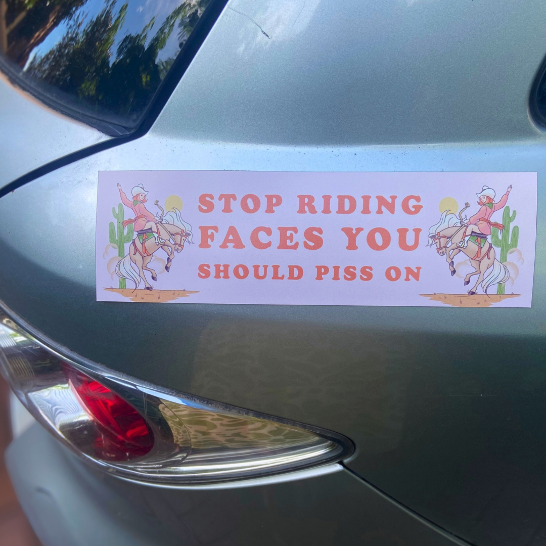 magnetic bumper sticker that says stop riding faces you should piss on in orange writing. Featuring a cowgirl illustration. Shop Feminist Trash for funny bumper stickers and feminist car magnets