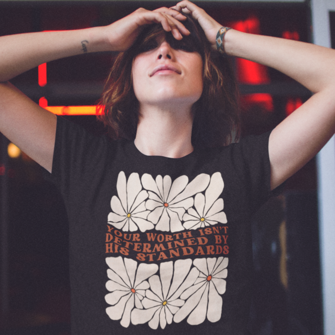 Black feminist shirt that says Your Worth Isn’t Determined By His Standards featuring a retro floral design- Shop Women’s Rights T-shirts and women's march merchandise