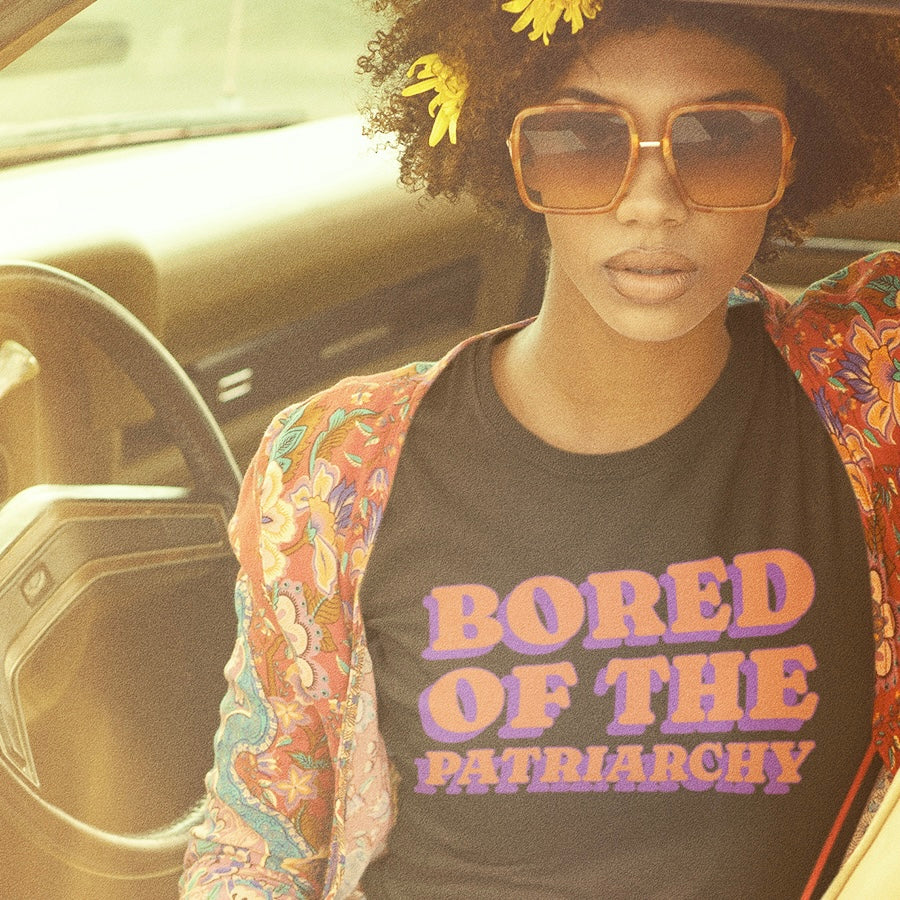 black feminist shirt that says bored of the patriarchy in orange and purple retro writing- Shop feminist trash, one of the best online stores to buy feminist shirts and political clothing.