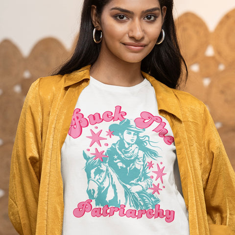 white feminist cowgirl tshirt that says buck the patriarchy in pink retro writing,, featuring a blue digital illustration of a cowgirl and a horse. Shop feminist trash store for feminist tees and political clothes