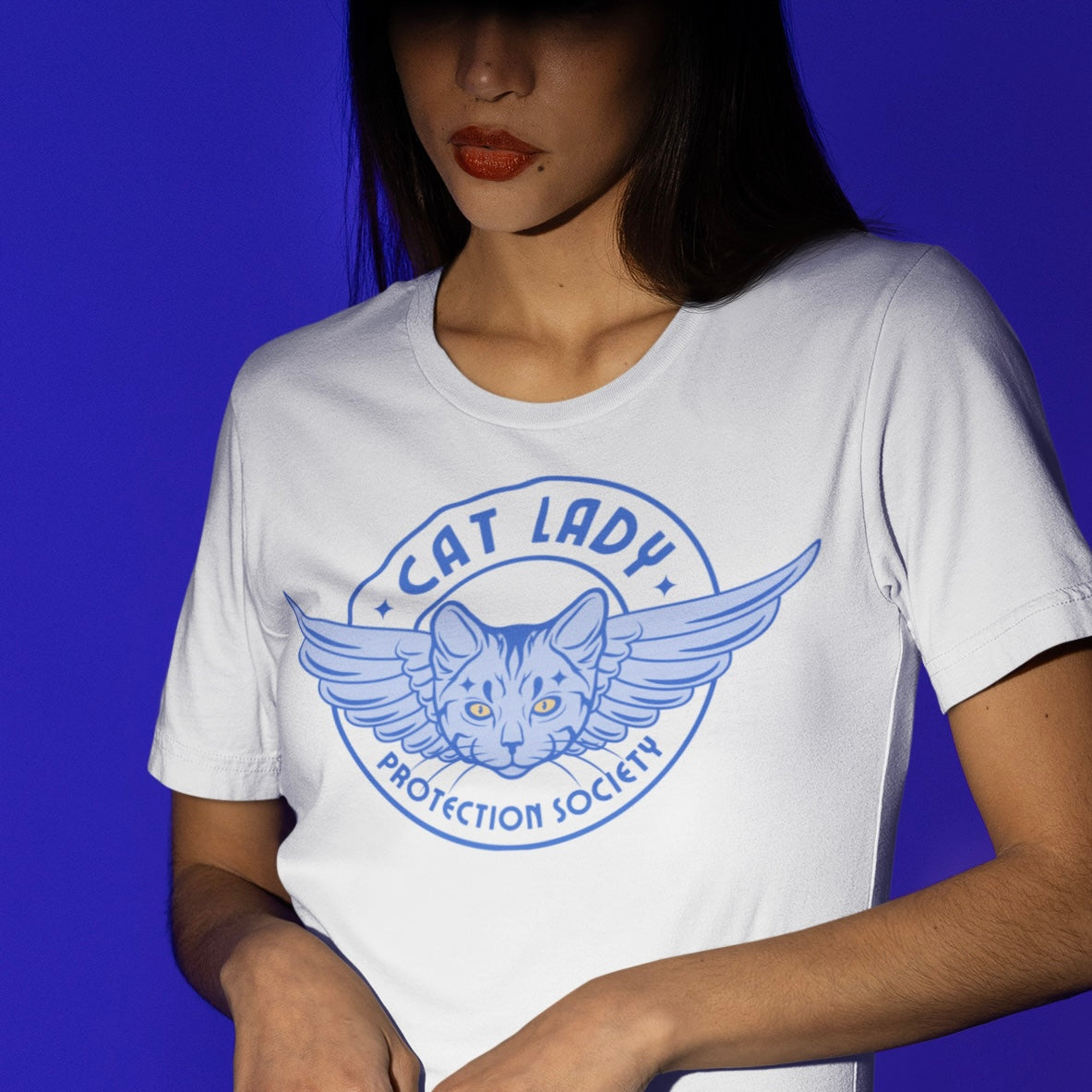 white cat lady tshirt that says cat lady protection society in blue writing, featuring and angel cat head emblem. Shop feminist Trash for feminist t-shirts and dump him shirts