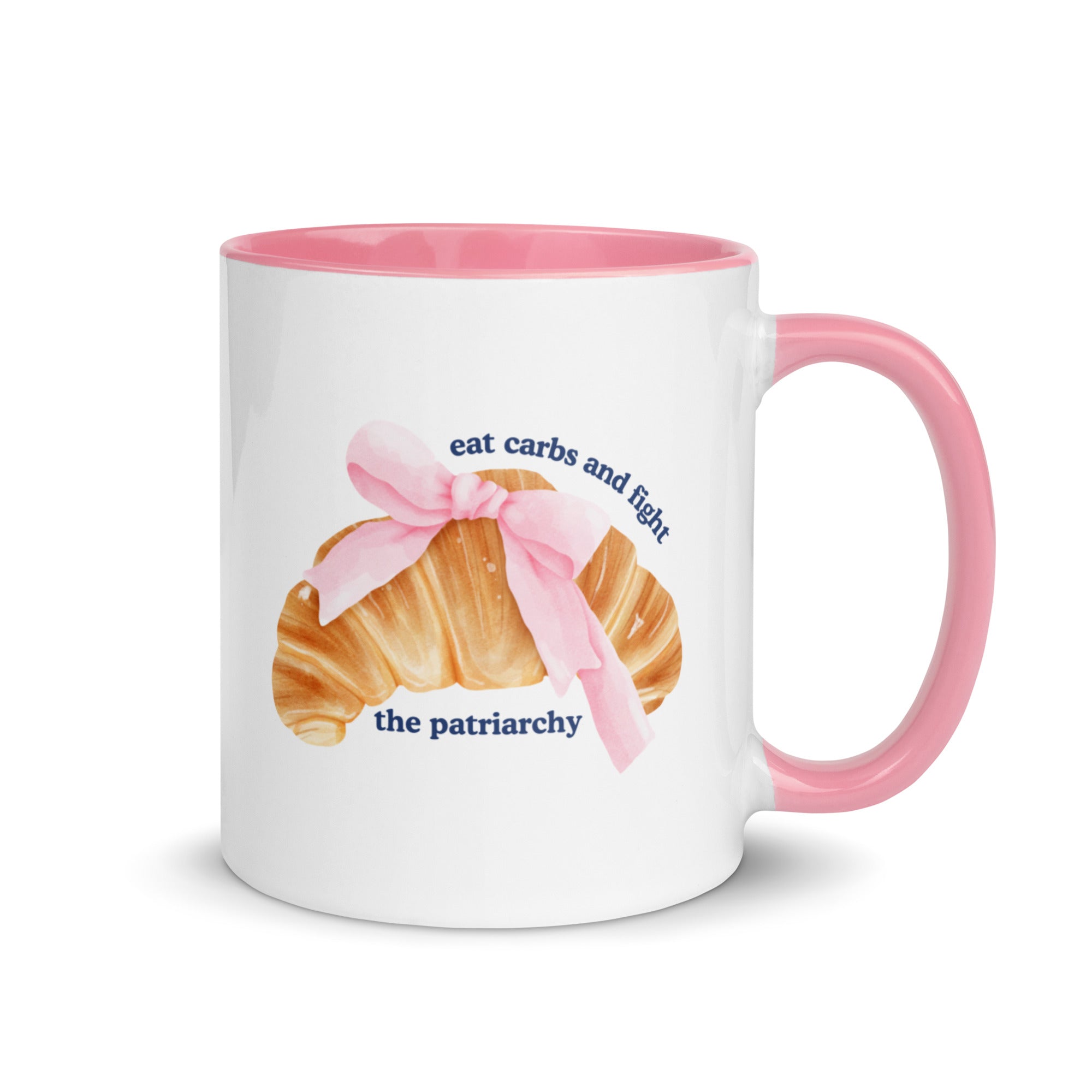 pink and white feminist mug featuring the phrase eat carbs and fight the patriarchy in navy writing and a coquette croissant illustration. Shop feminist trash store for feminist ceramics, political clothes and dump him shirts.
