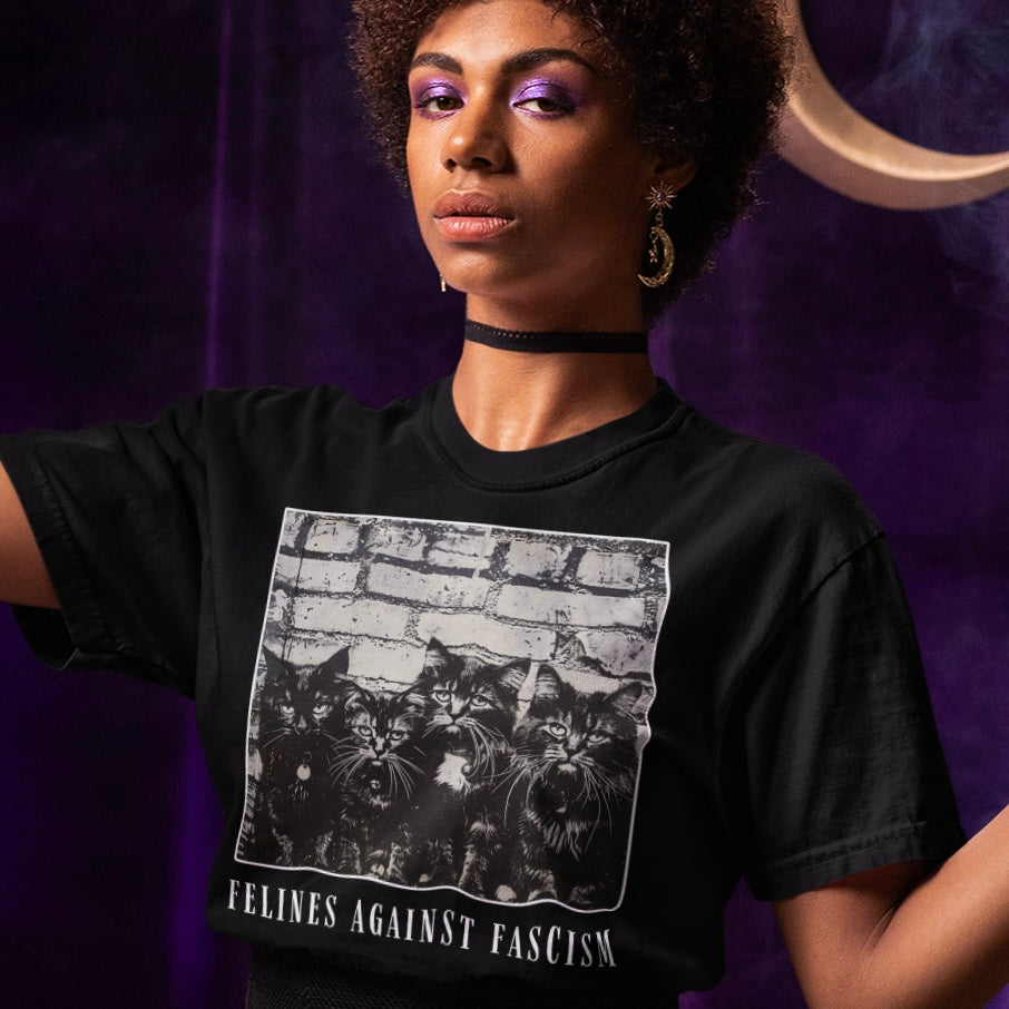black political t-shirt that says felines against fascism in white writing- featuring a group of cats against a white brick wall. shop feminist trash for political clothing and witchy outfits