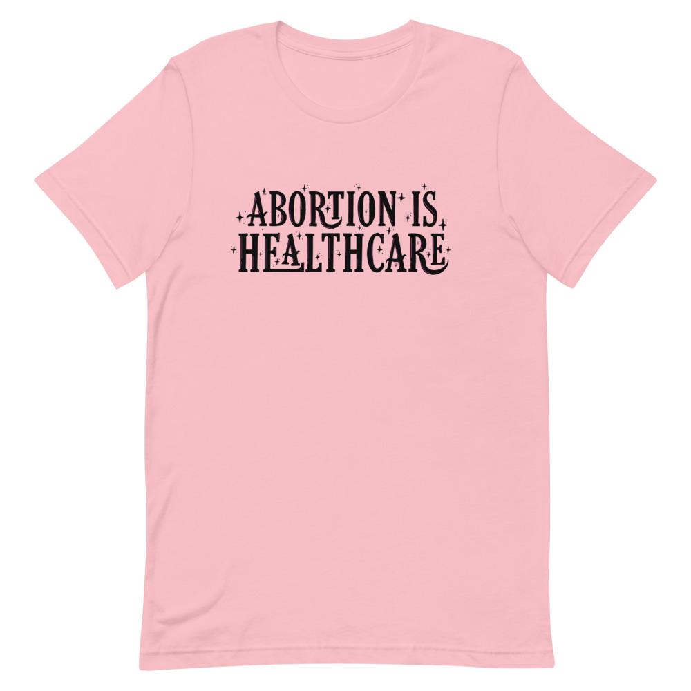 Pink feminist shirt advocating 'Abortion is Healthcare' in black hand lettering- Shop feminist tees.