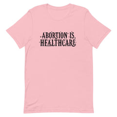 Pink feminist shirt advocating 'Abortion is Healthcare' in black hand lettering- Shop feminist tees.