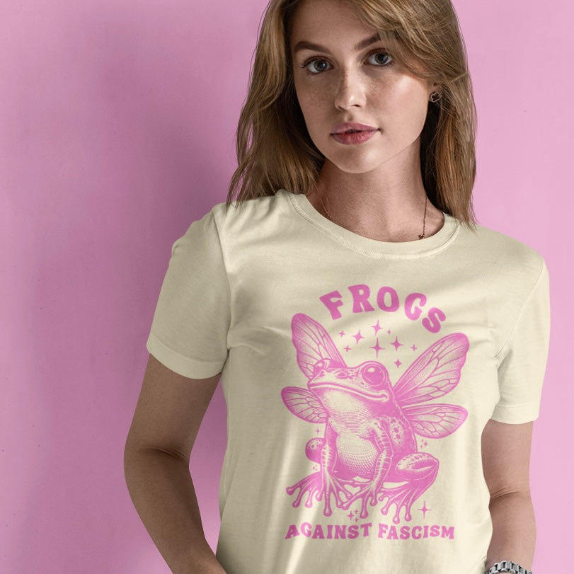 natural coloured political tee that says frogs against fascism in pink retro writing featuring a pink illustration of a frog with butterfly wings. Shop Feminist Trash for political clothing and acab t-shirts