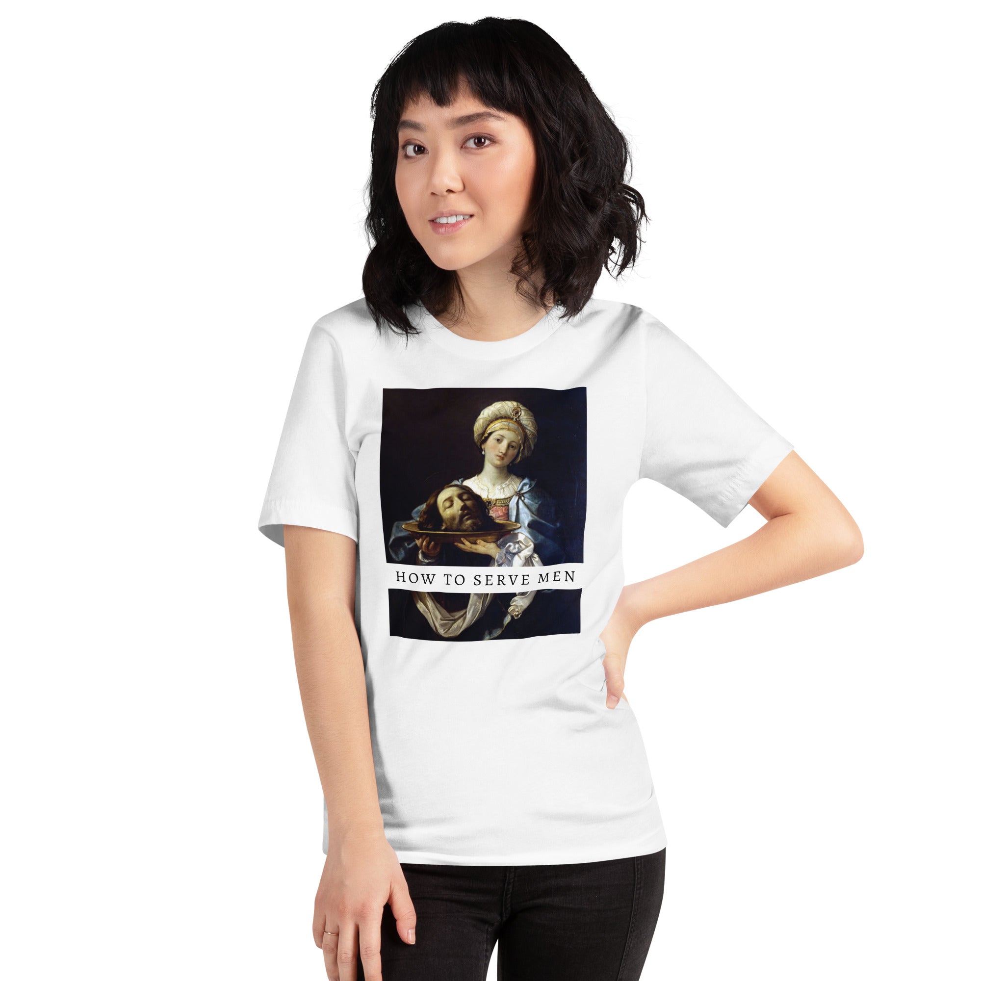 A woman with dark hair stands with her hand on her hip, modeling the white version of the How to Serve Men feminist shirt paired with black skinny jeans. Styled for a casual, streetwear activist look.