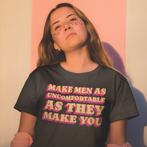 black feminist tee that says make men as uncomfortable as they make you in yellow and pink retro writing- shop feminist trash for feminist apparel and dump him shirts