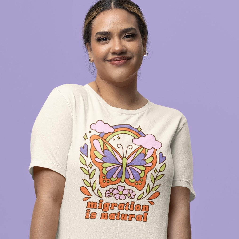 vintage white political tshirt that says migration is natural in orange retro writing- featuring a psychedelic butterfly illustration. Shop Feminist Trash Store for political clothing and leftist t-shirts