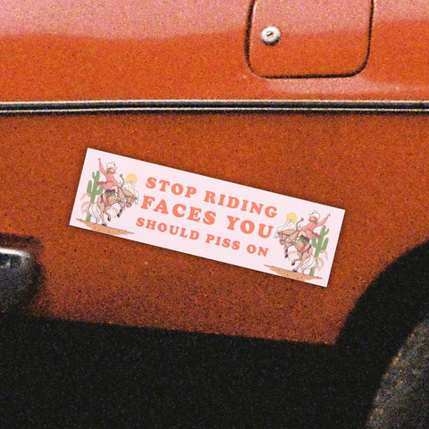 magnetic bumper sticker that says stop riding faces you should piss on in orange writing. Featuring a cowgirl illustration. Shop Feminist Trash for funny bumper stickers and feminist car magnets