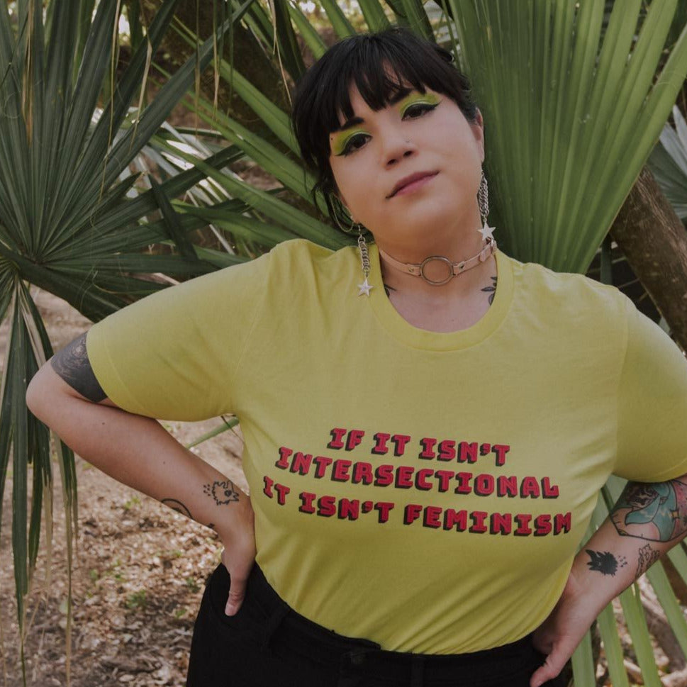 Yellow feminist t shirt with 'If It Isn’t Intersectional It Isn’t Feminism' text in red, promoting an inclusive message of empowerment and equality. Shop feminist apparel, dump him shirts, witchy outfits, political clothing and pride outfits.