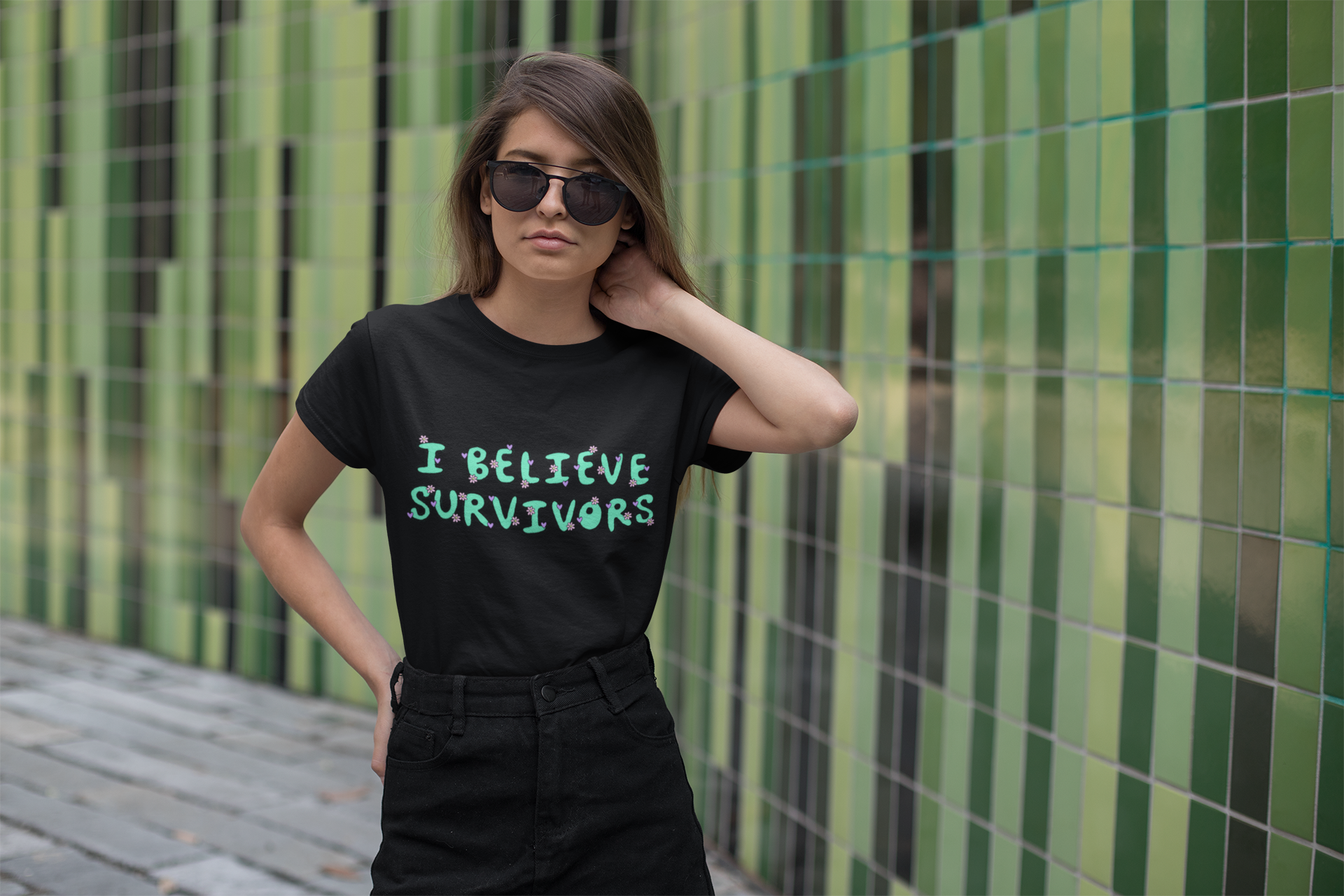 black feminist t-shirt that says believe survivors in green bubble writing with tiny purple daisy illustrations. Shop Feminist Trash for political clothing, pride outfits, feminist apparel, dump him shirts and witchy outfits