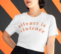 White feminist shirt that says silence is violence in bold orange lowercase writing- shop feminist shirts