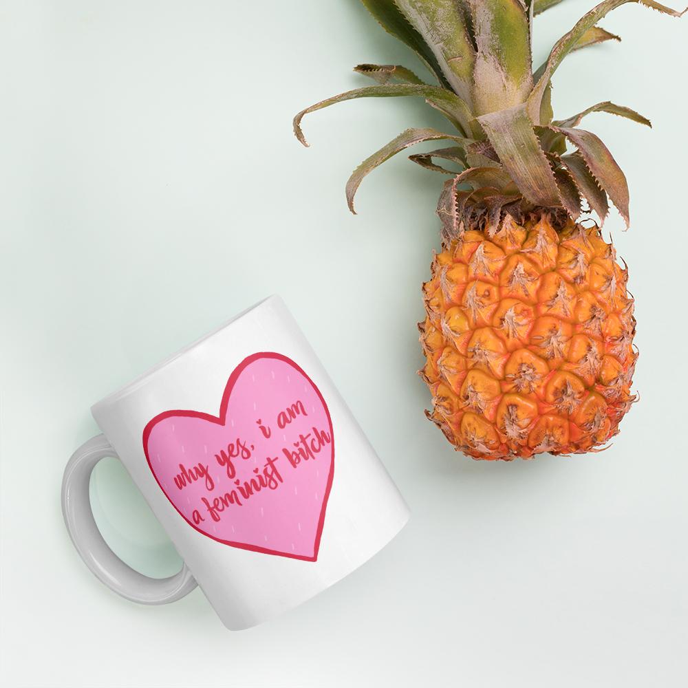 11 oz feminist mug that says Why Yes I am A Feminist Bitch in red writing inside a pink heart- shop feminist trash for feminist apparel, political clothing and dump him shirts