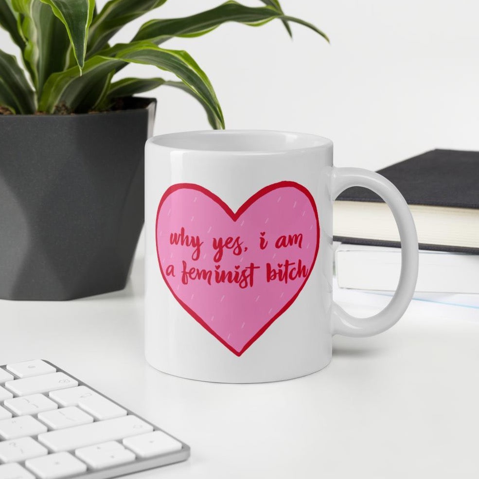 feminist mug that says Why Yes I am A Feminist Bitch in red writing inside a pink heart- shop feminist trash for feminist apparel, political clothing and dump him shirts