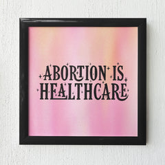 Feminist art print with the phrase "Abortion is Healthcare" in black hand-lettered writing, set against a gradient pink and orange background.- Shop Art Prints For The Empowered Woman