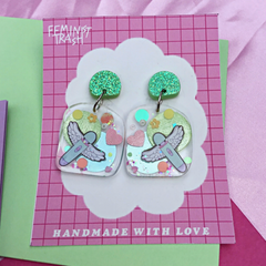 Feminist Earrings made out of resin featuring a cute baby blue vibrator with angel wings illustration and sparkly green elements