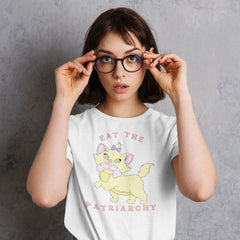 white feminist shirt that says eat the patriarchy in peach writing. featuring a cute cat illustration with a penis in it's mouth- Shop feminist apparel