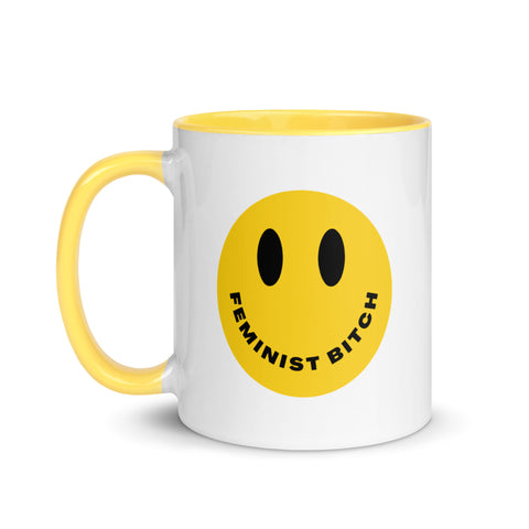 white and yellow feminist mug that says feminist bitch inside a yellow retro smiley face- shop feminist trash for feminist ceramics and political clothing.