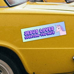 Funny political magnetic bumper sticker that says Jesus loves everyone you hate in purple writing, featuring a purple unicorn illustration. Shop feminist trash store for funny bumper stickers and political clothes.