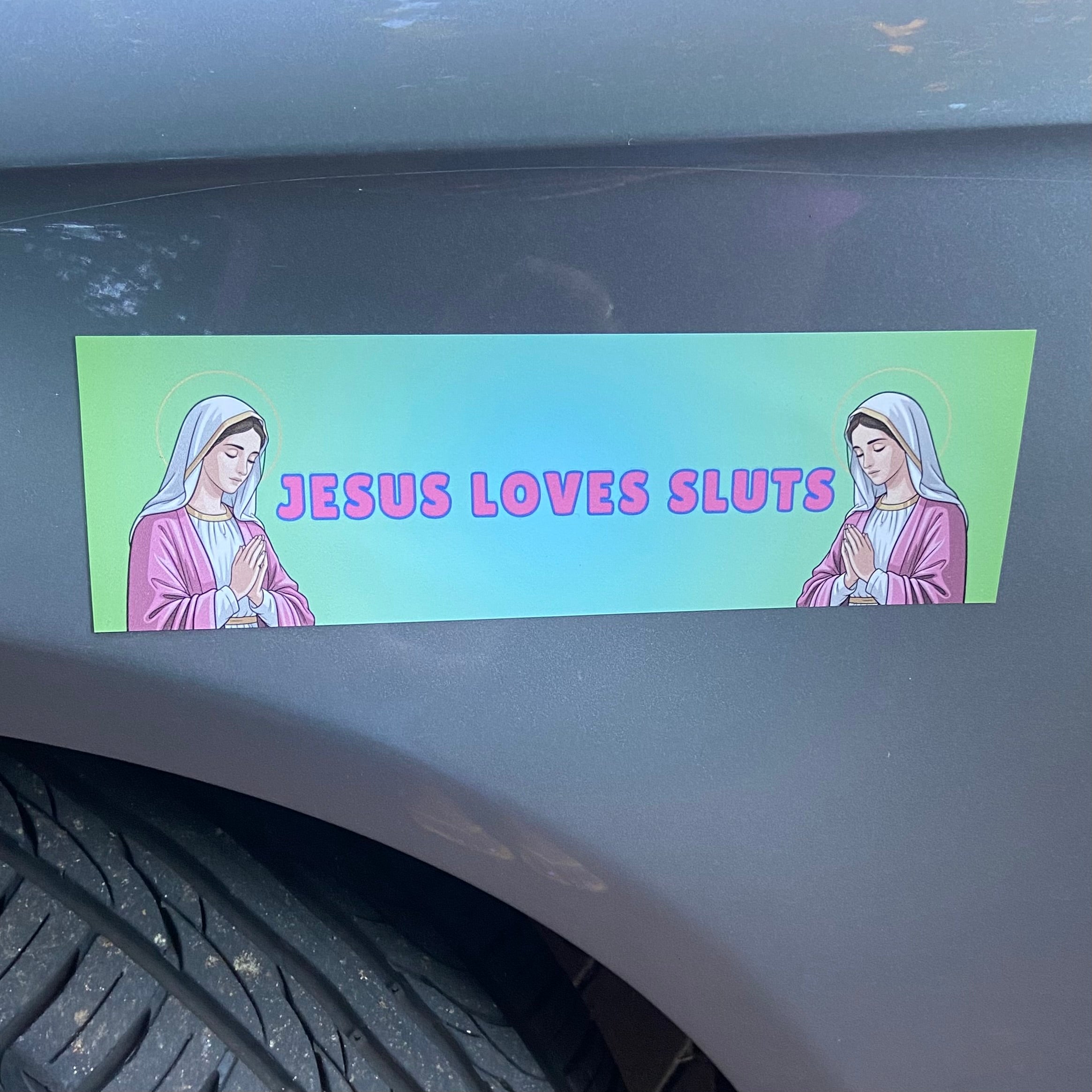 Magnetic Bumper Sticker with cartoon characters of Mary Magdalene and 'JESUS LOVES SLUTS' text in pink writing- shop feminist trash for funny bumper stickers and women’s March merchandise.