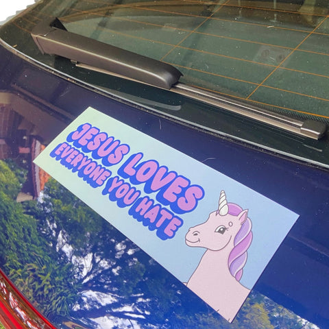 Funny political magnetic bumper sticker that says Jesus loves everyone you hate in purple writing, featuring a purple unicorn illustration. Shop feminist trash store for funny bumper stickers and political clothes.