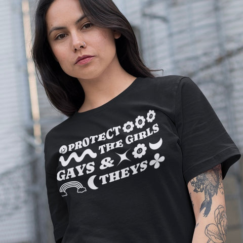 Black pride shirt that says girls gays and theys in white retro writing featuring cute retro graphics like smiley flowers and rainbow. Shop feminist trash store for outfits for pride, political t-shirts and feminist apparel