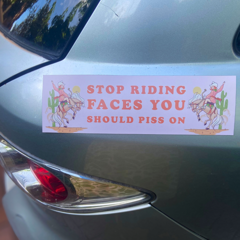 magnetic bumper sticker that says stop riding faces you should piss on in orange writing. Featuring a cowgirl illustration. Shop Feminist Trash for funny bumper stickers and feminist car magnets