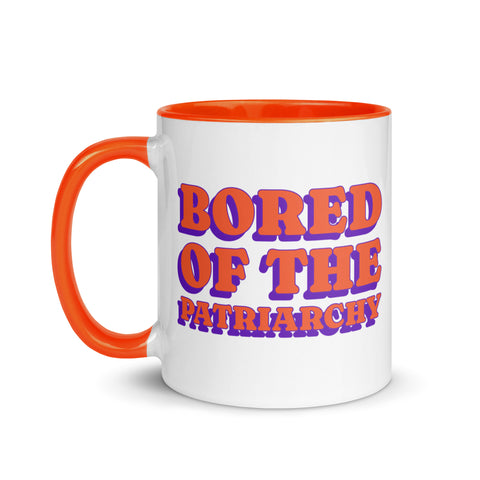 white and orange feminist mug that says bored of the patriarchy in orange and purple writing- shop feminist trash for feminist ceramics, political tees and outfits for pride