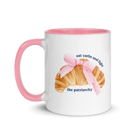 pink and white feminist mug featuring the phrase eat carbs and fight the patriarchy in navy writing and a coquette croissant illustration. Shop feminist trash store for feminist ceramics, political clothes and dump him shirts.