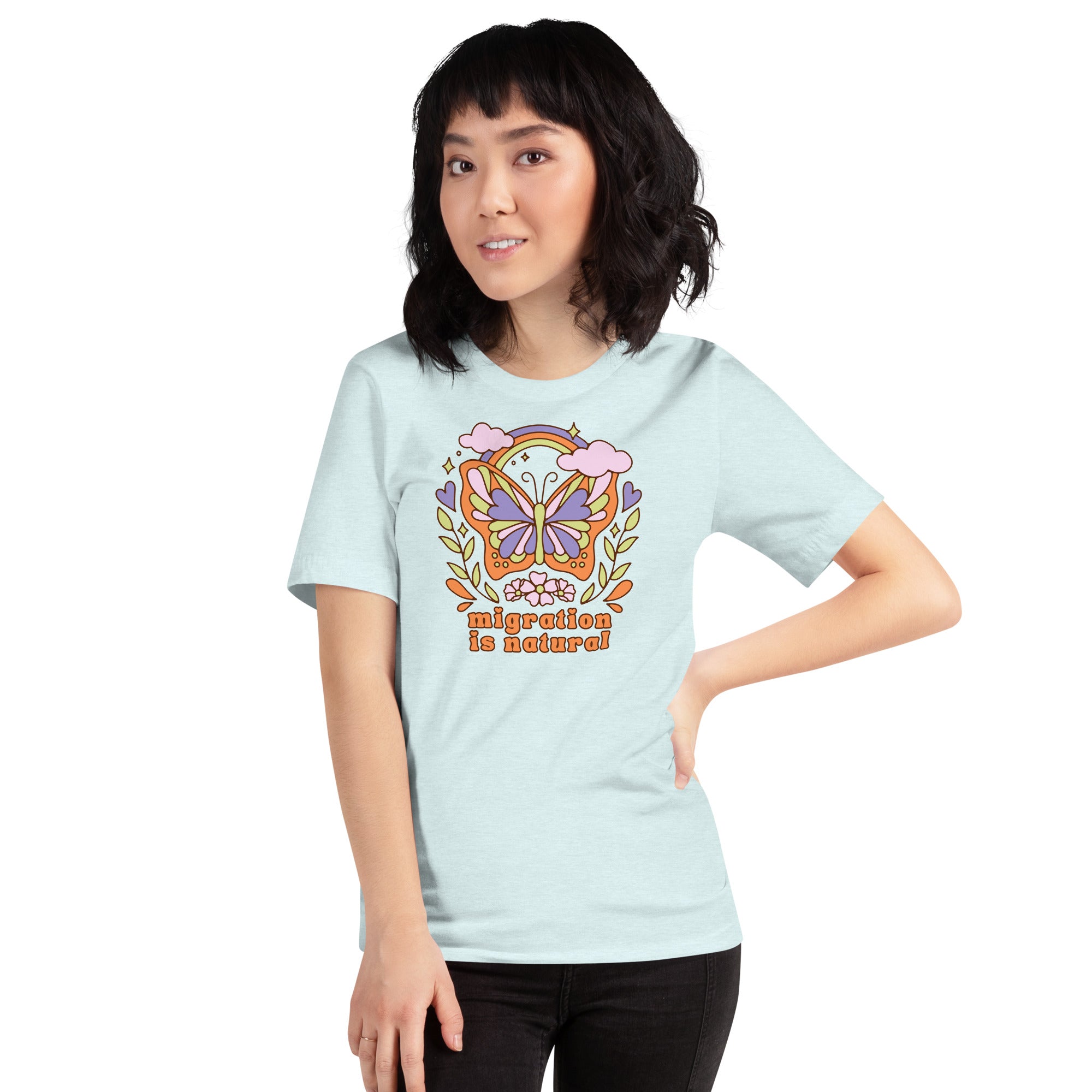 A person with dark hair wearing the light blue migration is natural butterfly political t-shirt paired with black pants against a white background.