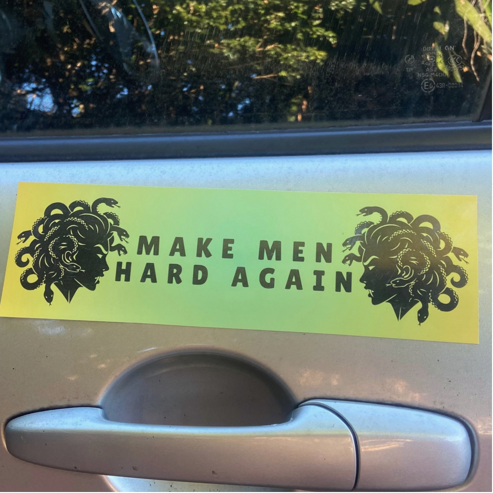 A funny feminist car magnet in neon green-yellow featuring the text "MAKE MEN HARD AGAIN" flanked by two black Medusa illustrations