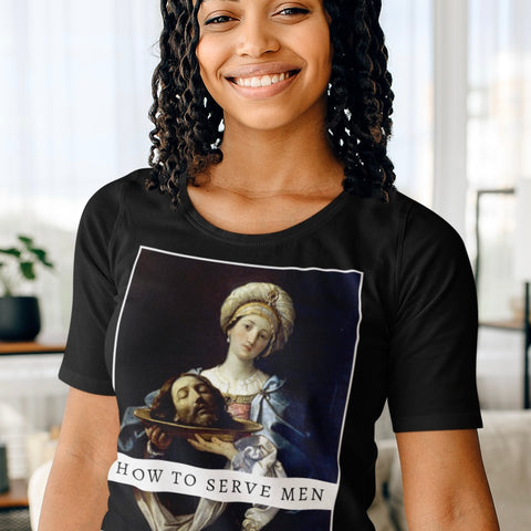 Close-up of a smiling woman wearing the black How to Serve Men graphic feminist t-shirt. The shirt features the Baroque painting Salome with the Head of John the Baptist by Guido Reni, blending fine art with a bold feminist statement.