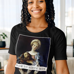 Close-up of a smiling woman wearing the black How to Serve Men graphic feminist t-shirt. The shirt features the Baroque painting Salome with the Head of John the Baptist by Guido Reni, blending fine art with a bold feminist statement.