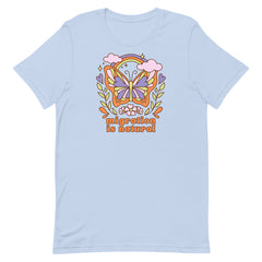 Flat lay of a baby blue t-shirt featuring a colorful retro butterfly illustration with a rainbow and clouds above the text migration is natural in orange groovy typography