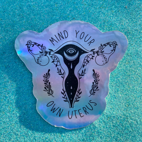 holographic feminist sticker that says mind your own uterus featuring a witchy uterus illustration- shop feminist trash for feminist stickers and political pins
