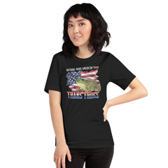 A smiling model with short dark hair wearing the black Nothing More American Than Trans Frogs Shirt. The funny pride t shirt features a green bullfrog graphic overlaid on a distressed American flag background