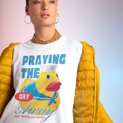 A person wearing the white Feminist Trash queer pride shirt that says praying the gay away just makes us gayer styled underneath a bright yellow puffer jacket with a gold chain necklace