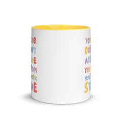 Feminist message mug with yellow handle and colorful block text about domestic labor, isolated on a white background.