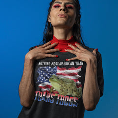 Close up look at a person modeling the black Trans Frogs Shirt From Feminist Trash,  layered over a bright red mock neck turtleneck. The individual has bold red eye makeup and matching red nails against a solid blue background. 