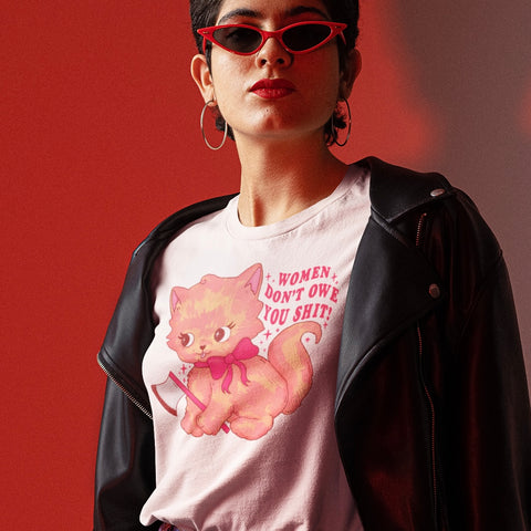 White feminist t-shirt featuring 'Women don’t owe you shit' in bold red, complemented by a cute cat holding a knife illustration. Add this feminist shirt to your wardrobe today. Shop Feminist Trash for funny feminist tees and political clothing.