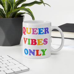11 oz Pride mug that says Queer Vibes in rainbow retro writing- shop feminist trash for pride clothing, political t shirts, feminist apparel and dump him shirts