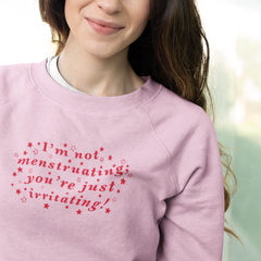 Pink feminist sweatshirt that says I’m Not Menstruating You’re Just Irritating in red wavy writing with stars surrounding it- define feminism with our feminist apparel